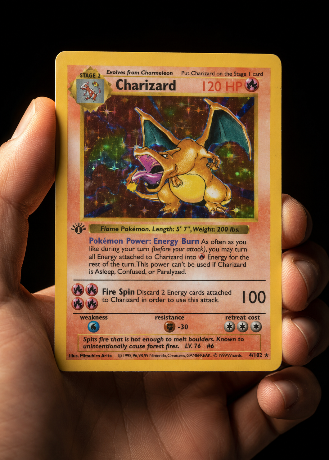 A Charizard Pokémon trading card held in a person's hands against a black background. The card is yellow-orange with artwork of a fire-breathing dragon and visible text including 'Charizard' and '120 HP'.