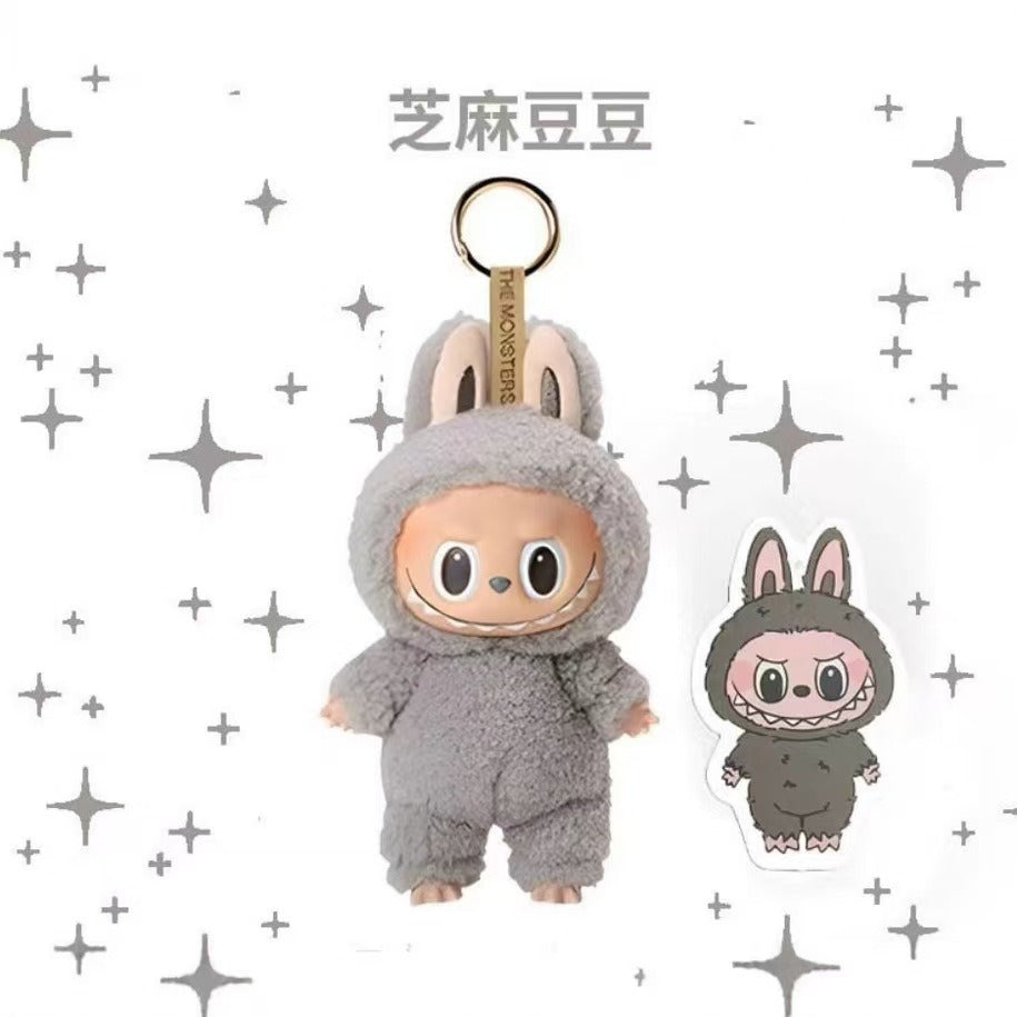 A plush character keychain in a gray bunny suit with a gold ring, shown alongside a small matching sticker on a white background with gray star graphics. The text above reads 福入品主.
