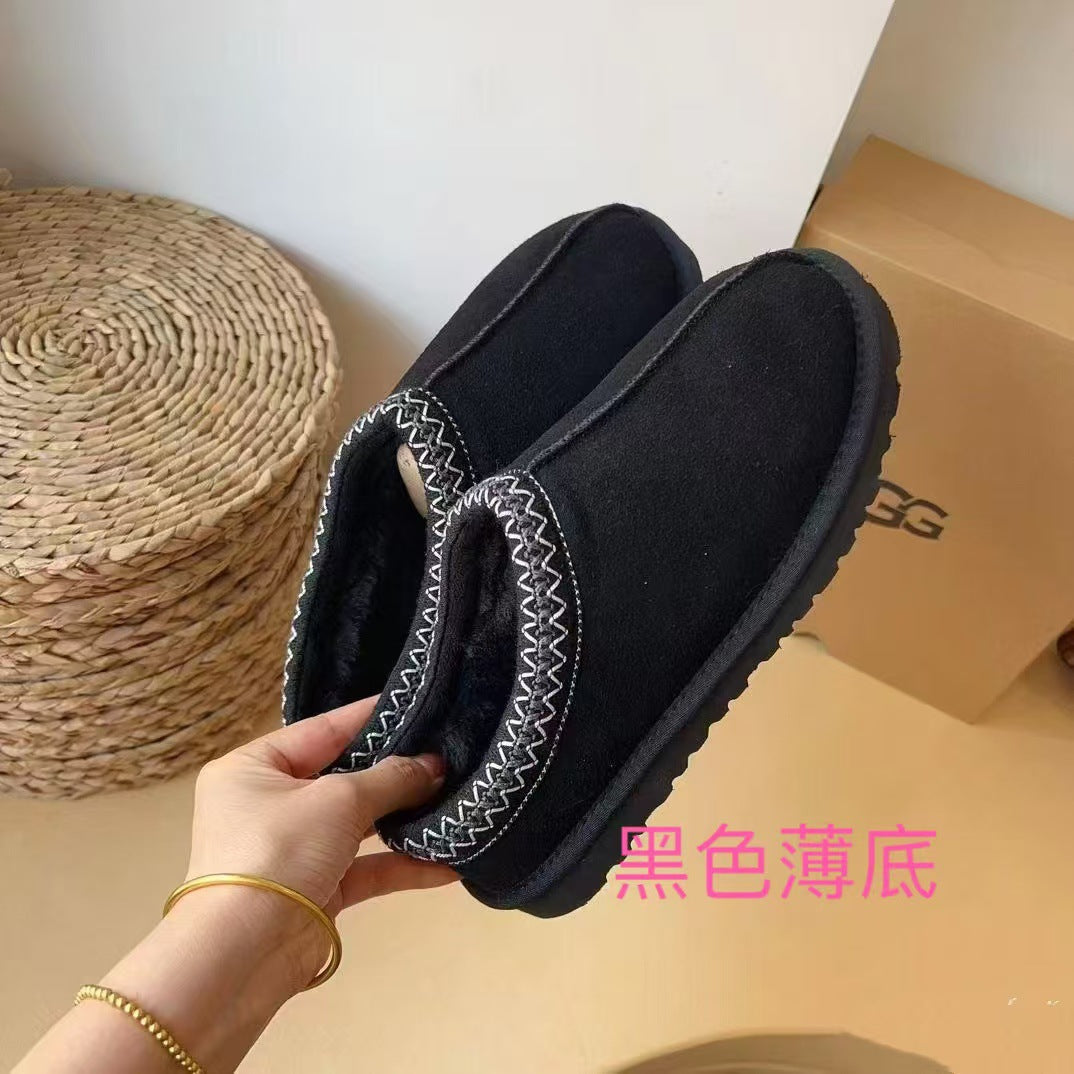 Black slippers with decorative elements held by a hand against a neutral background