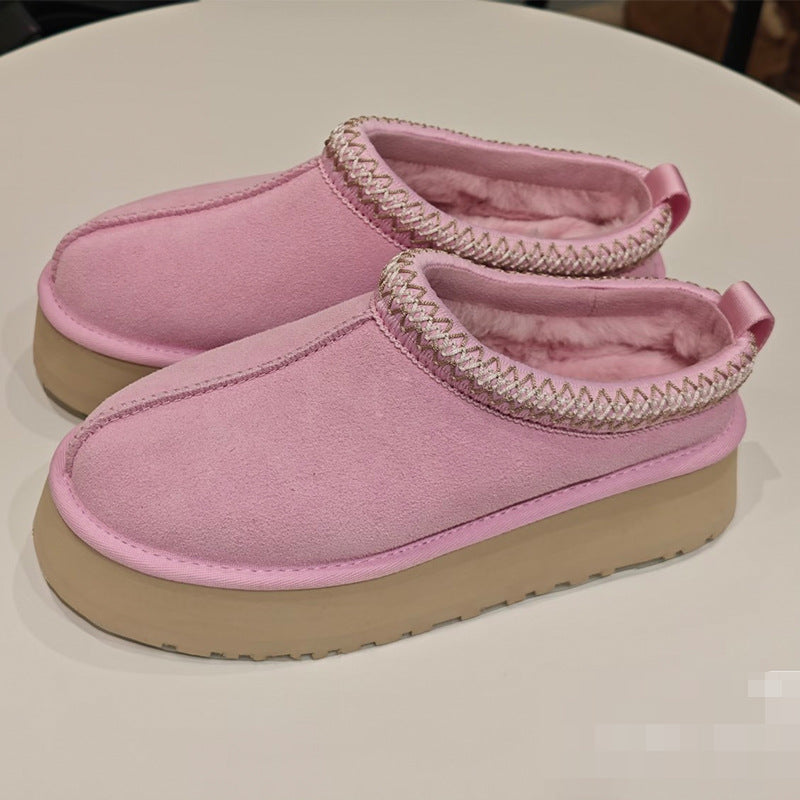A pair of pink slip-on slippers with a soft fleece lining, decorative braided trim around the collar, and thick tan platform soles, displayed on a light-colored surface.
