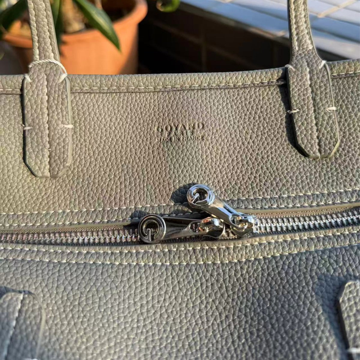 Gray handbag with a visible brand logo, zipper, and handle.