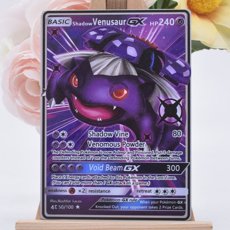 A Pokémon trading card featuring Shadow Venusaur GX, displayed upright on a small wooden stand with soft pink flowers blurred in the background.