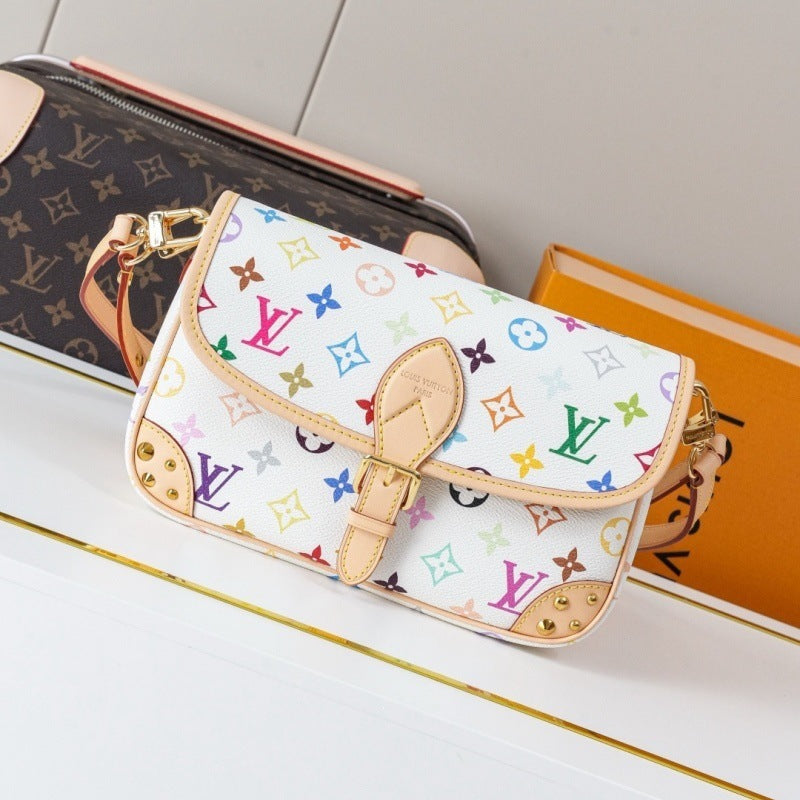 A Louis Vuitton monogram shoulder bag in white canvas with multicolor monogram motifs and tan leather trim, displayed on a white surface next to a brown monogram pouch and an orange box.