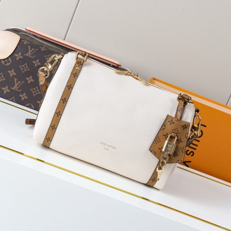 A Louis Vuitton monogram canvas and off-white leather zip pouch with gold-tone hardware, styled on a white shelf next to an orange book.