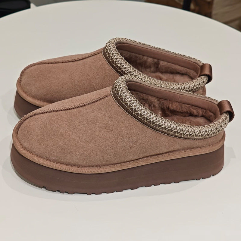 A pair of slip-on clog-style slippers in a warm taupe-brown suede-like material, featuring a thick dark brown sole, a textured beige-and-brown trim around the opening, and soft brown faux-fur lining visible inside.