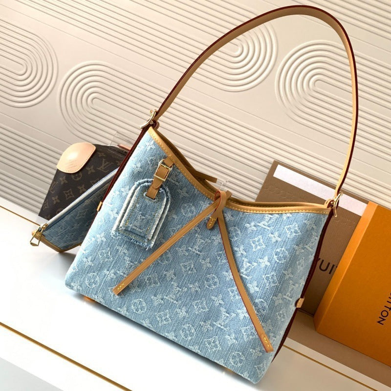 A light blue monogram canvas shoulder bag with tan leather trim and strap, displayed on a white surface with a Louis Vuitton box and another monogram bag in the background.