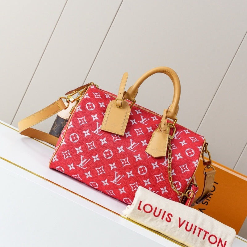 A red Louis Vuitton monogram handbag with tan leather handles and trim, displayed on a white surface with an orange box and a white dust bag in the foreground.