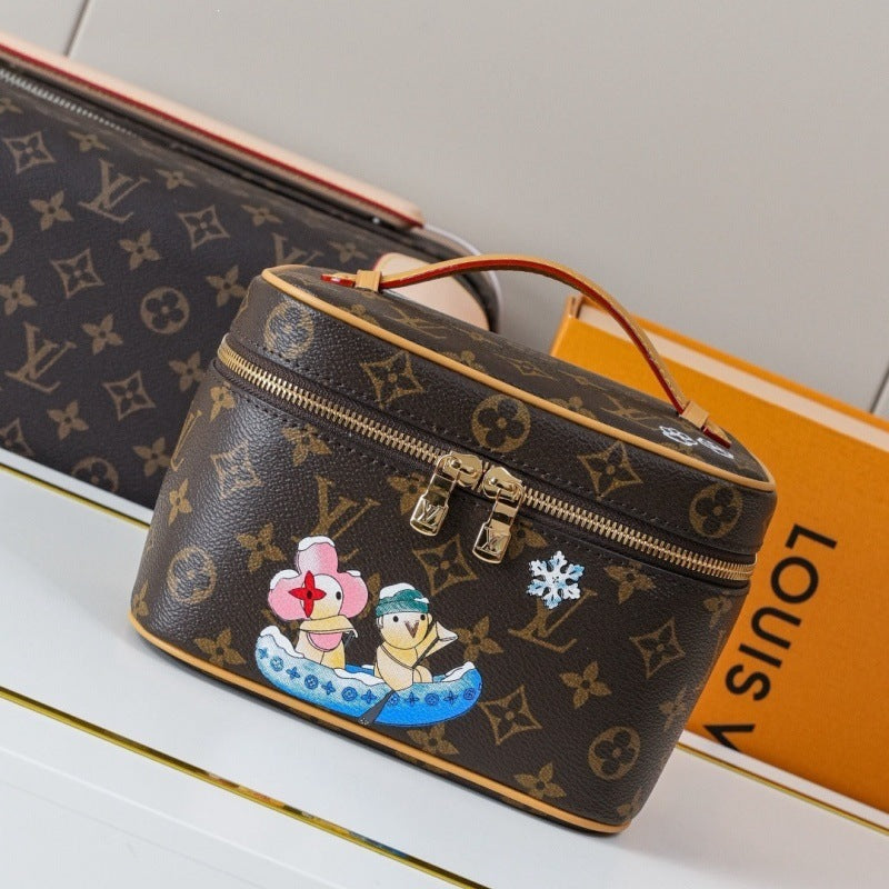 A Louis Vuitton monogram toiletry bag with a top zipper, brown leather handle, and cartoon character patches, shown on a white surface with a Louis Vuitton box in the background.