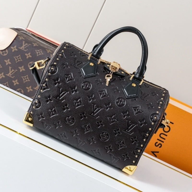 A Louis Vuitton black monogram embossed handbag with gold-tone hardware and top handles, displayed on a white surface with part of an orange Louis Vuitton box visible behind it.