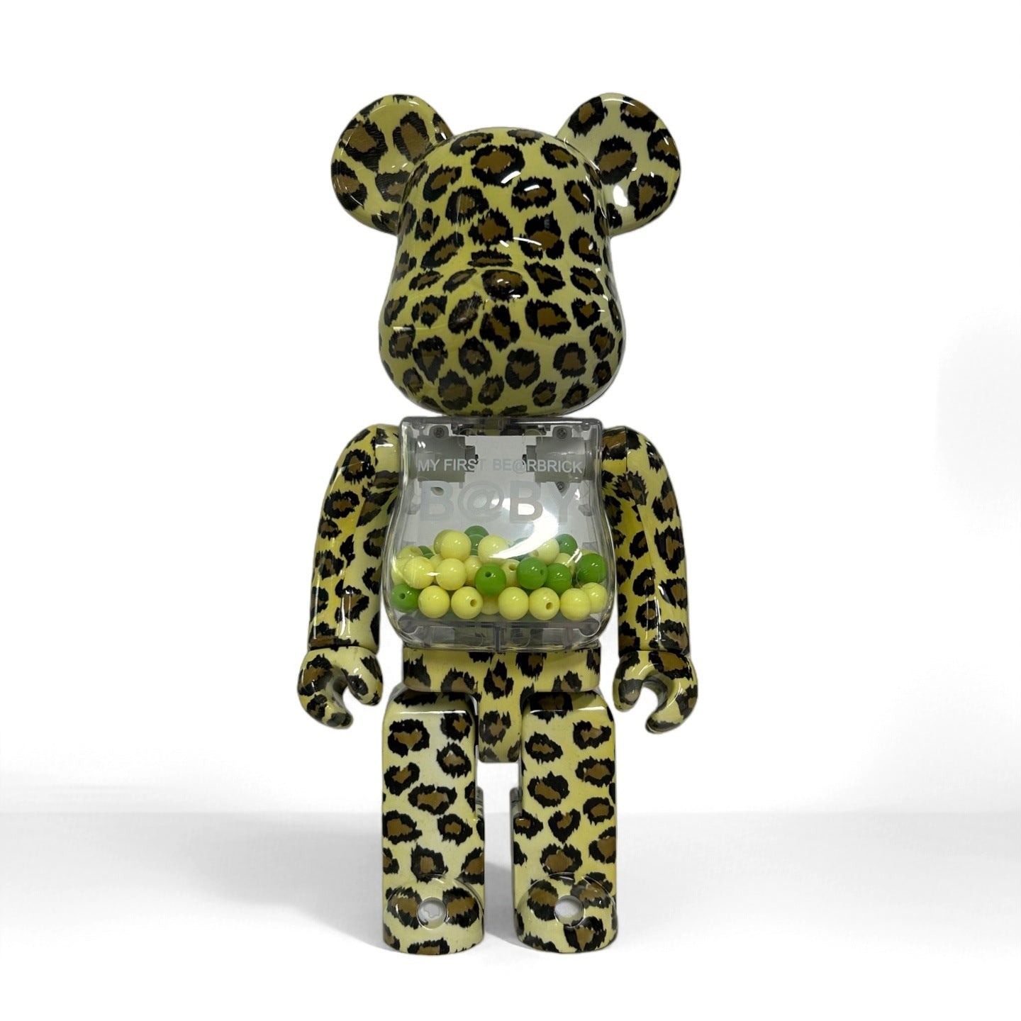A bear-shaped collectible figure with a green and black leopard print pattern, featuring a transparent chest compartment filled with small green and yellow beads, set against a plain white background.