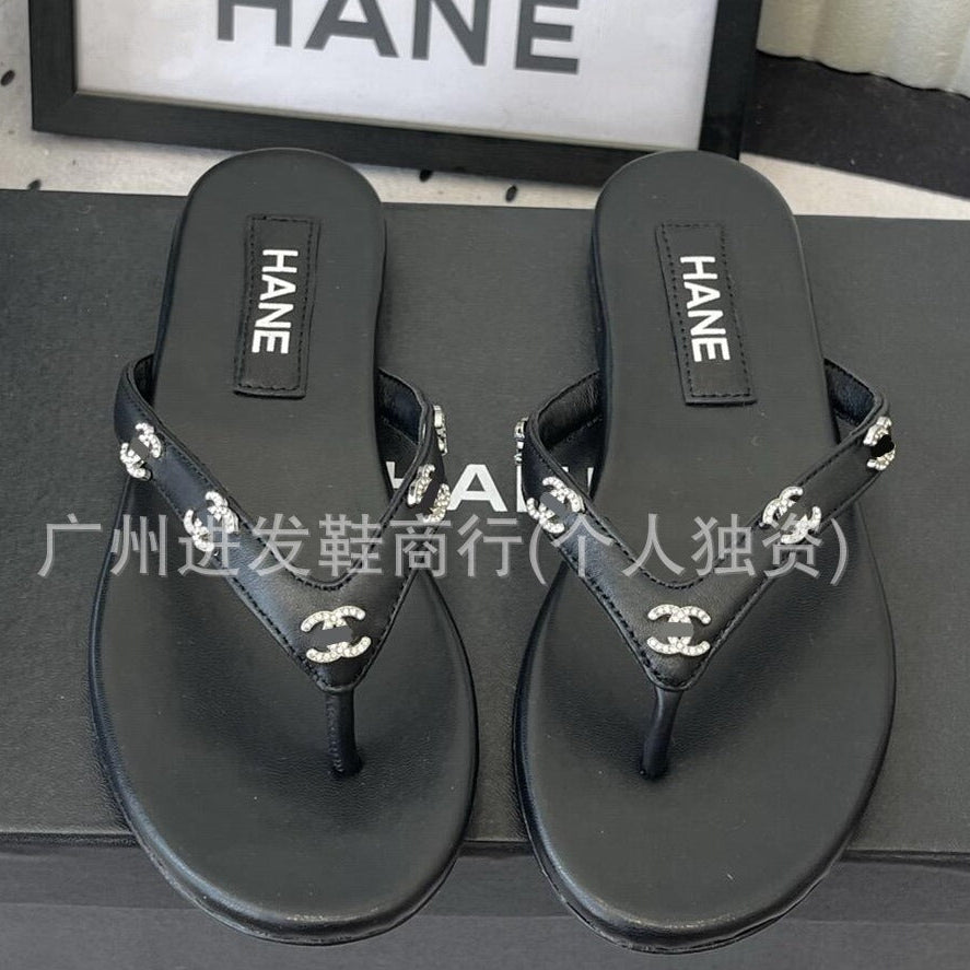 A pair of black Chanel flip-flop sandals with silver-tone interlocking CC logo embellishments on the straps, displayed on top of a black Chanel shoebox.