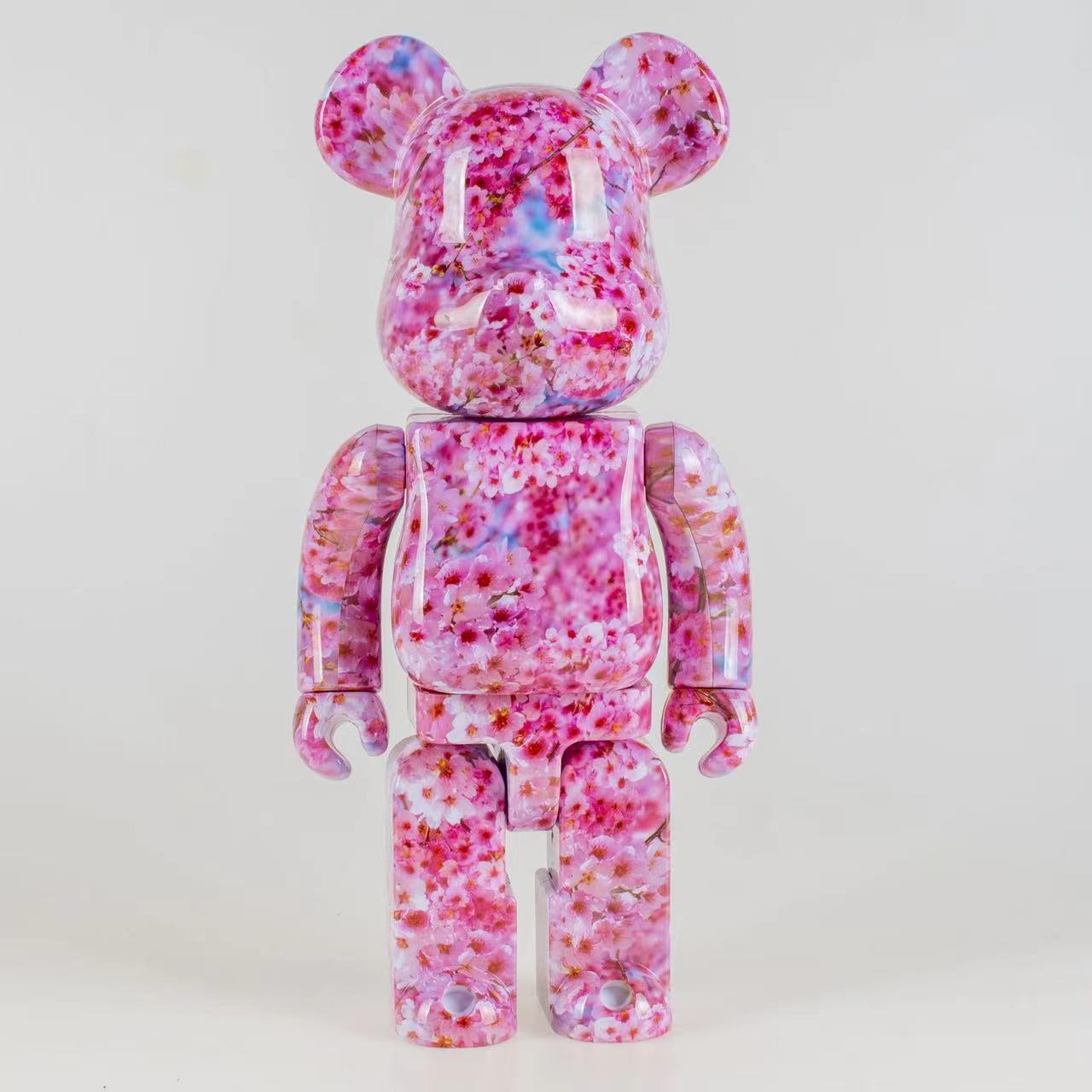A pink and white cherry blossom-patterned bear figure toy, photographed against a seamless white studio background.