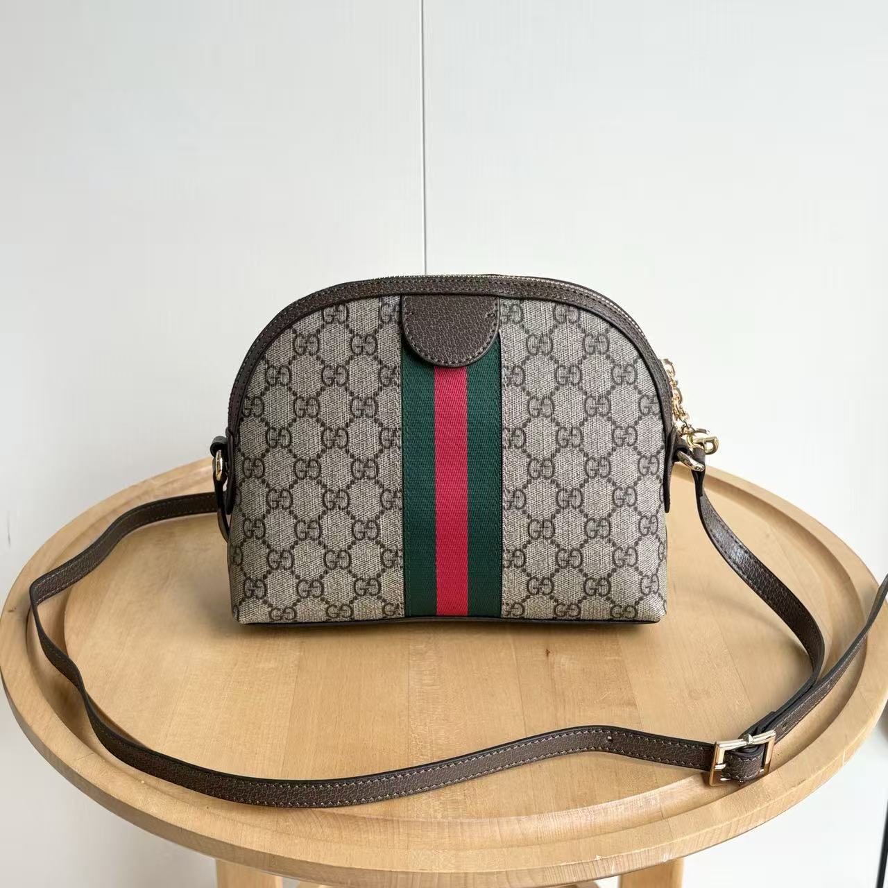 Designer handbag with patterned design and red and green stripe on a wooden table.