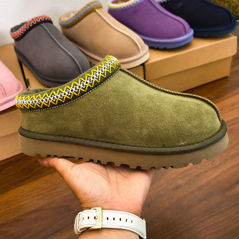 Green slip-on shoes being held by a hand on a wooden floor.
