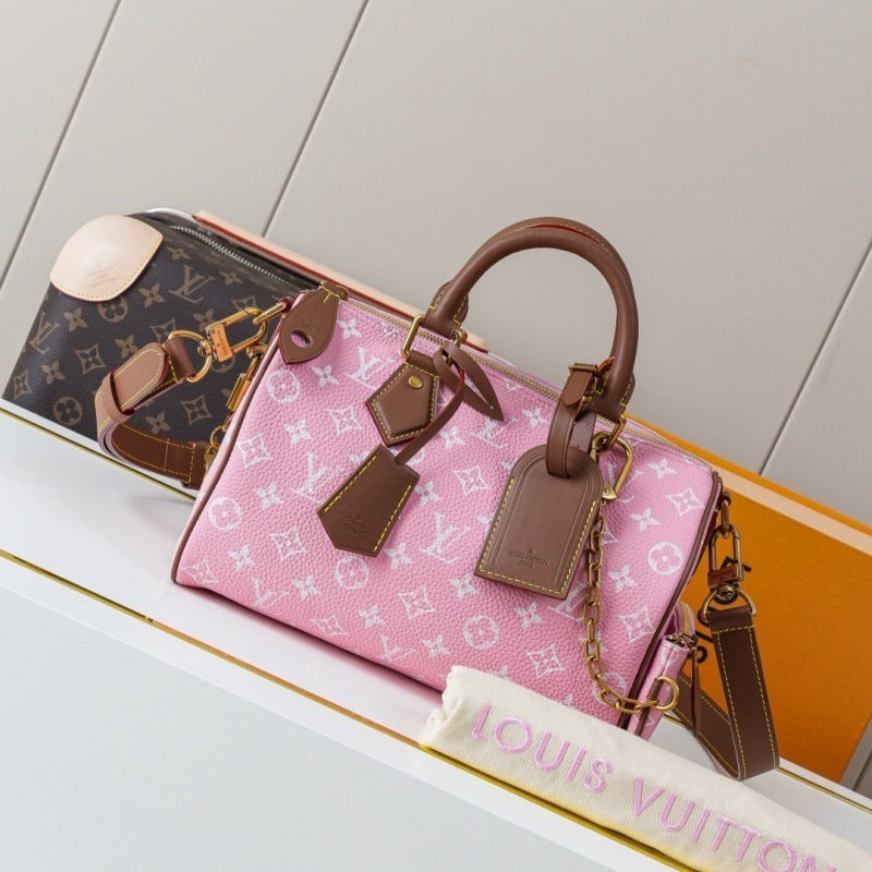 A pink Louis Vuitton monogram Speedy handbag with brown leather handles and trim, displayed on a white shelf alongside a brown Louis Vuitton monogram bag and an orange box.