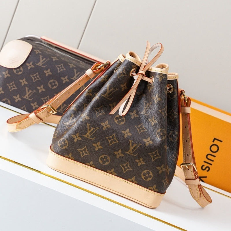 Louis Vuitton monogram canvas bucket bag with tan leather trim and drawstring closure, displayed on a white surface with a Louis Vuitton box in the background.
