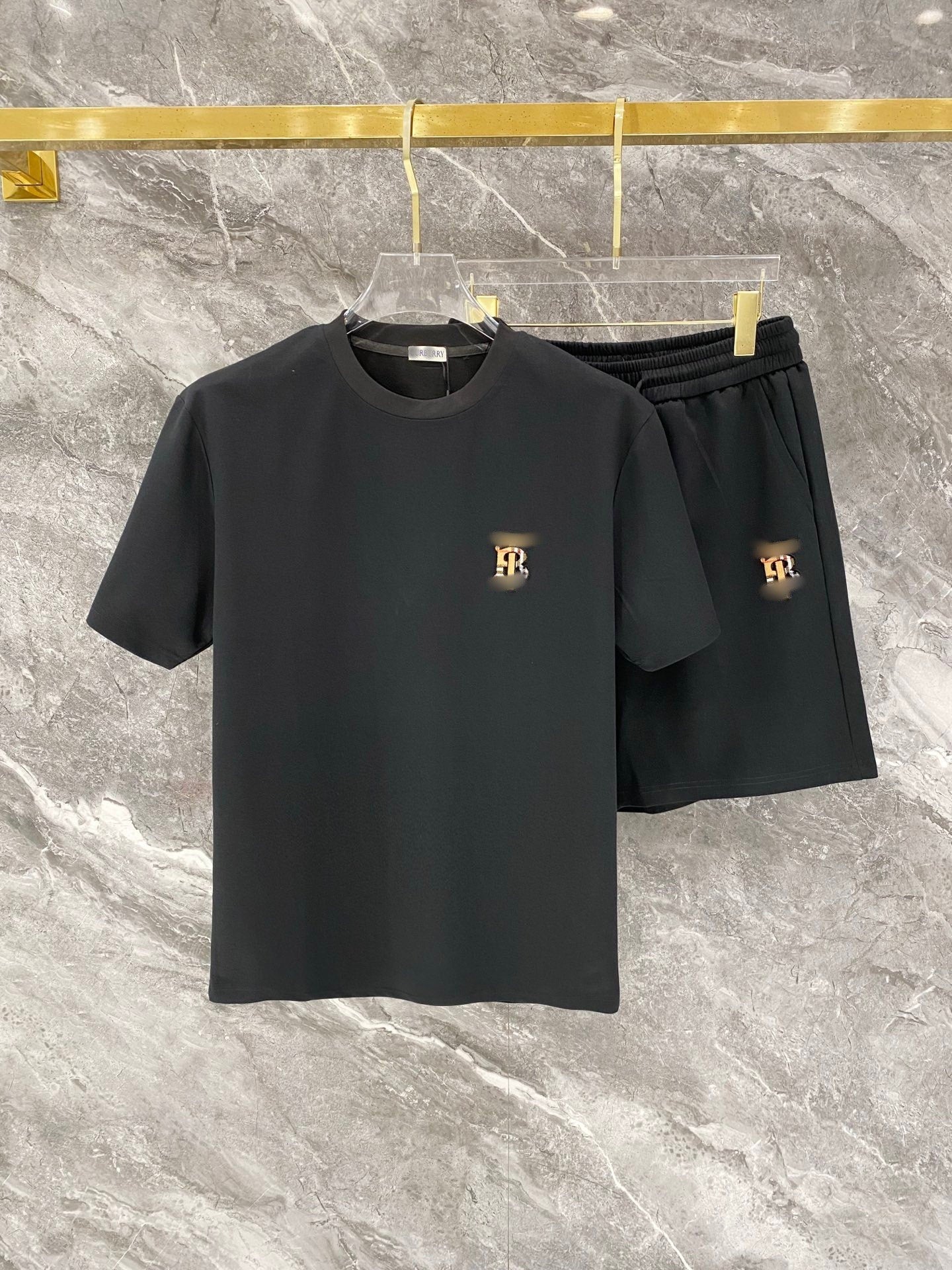 Black t-shirt and shorts set with gold logo on a marble surface