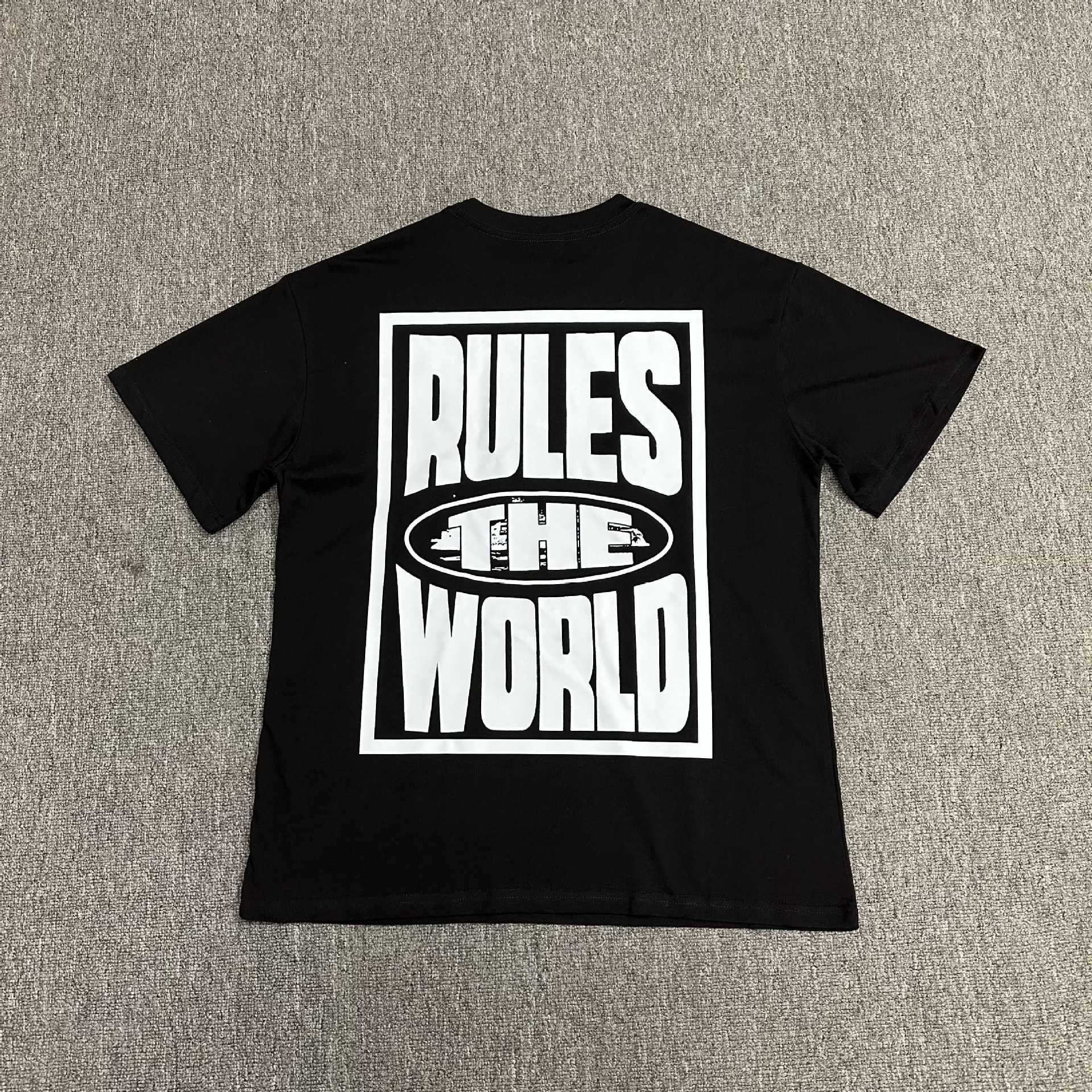 Black t-shirt with 'RULES THE WORLD' text on a gray surface