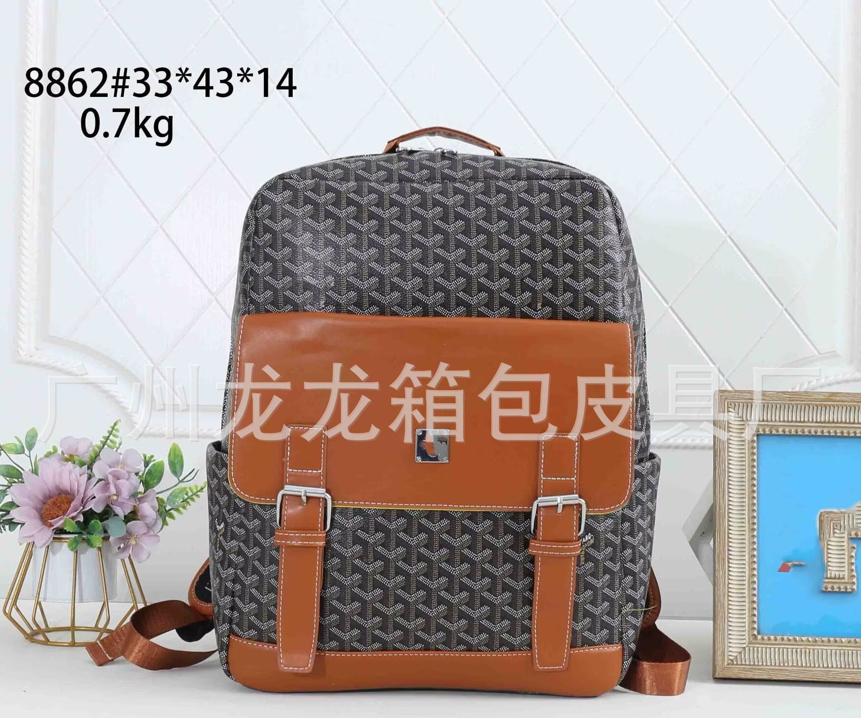 A Goyardine-patterned gray and brown backpack with tan leather trim and buckle straps, shown against a white paneled wall with decorative flowers and a picture frame. Text on the image includes '8862#33*43*14 0.