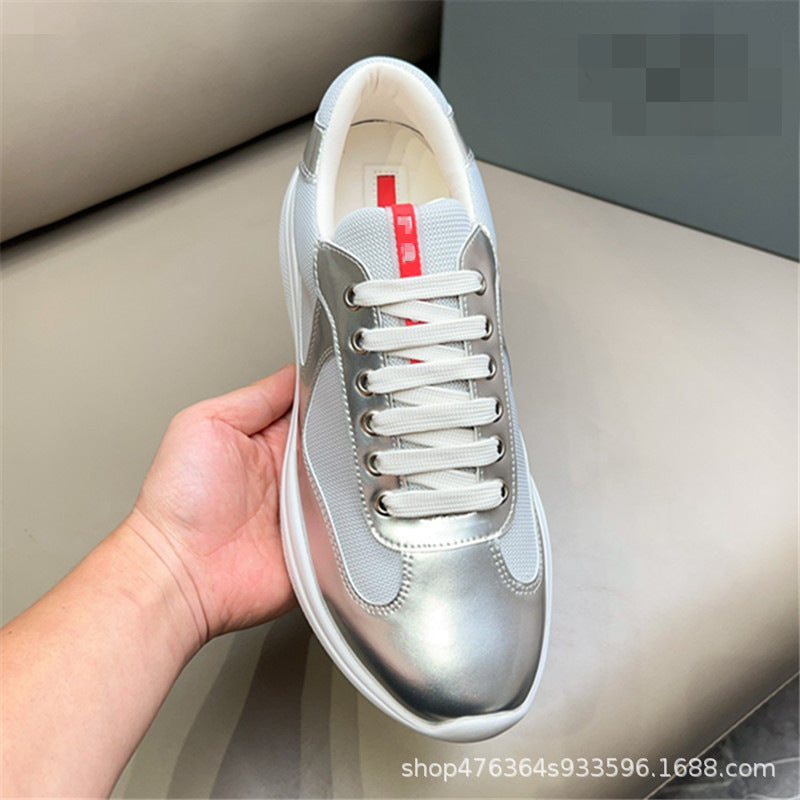 Silver sneaker with white laces held by a hand on a neutral background