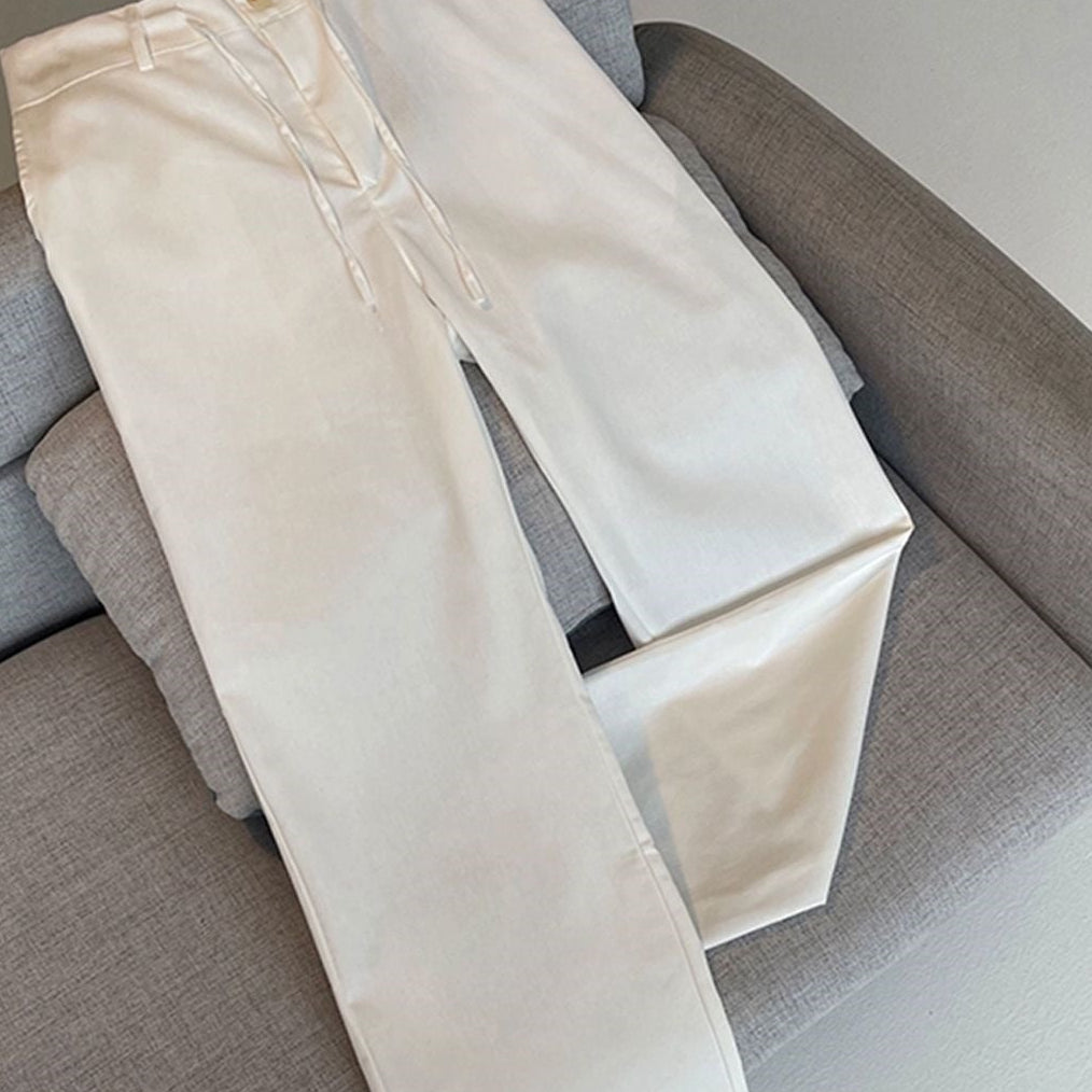 A pair of off-white or cream-colored slim-fit jeans laid flat on a gray upholstered chair, with Chinese promotional text overlays at the top and bottom.
