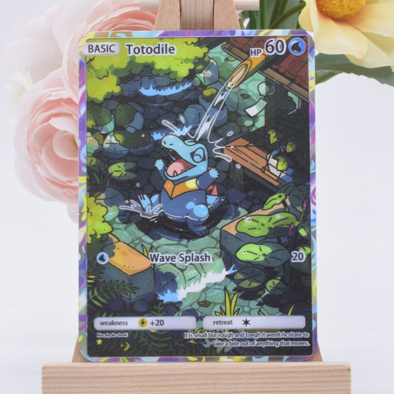 A holographic Pokémon trading card featuring the character Totodile, displayed on a small wooden stand with soft pink and yellow flowers blurred in the background.