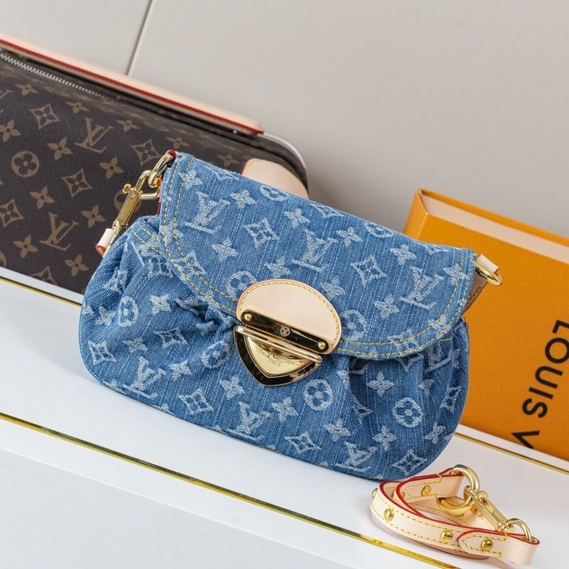 A Louis Vuitton monogram canvas shoulder bag in blue denim, styled on a white shelf with a Louis Vuitton box and a matching monogram pouch in the background.