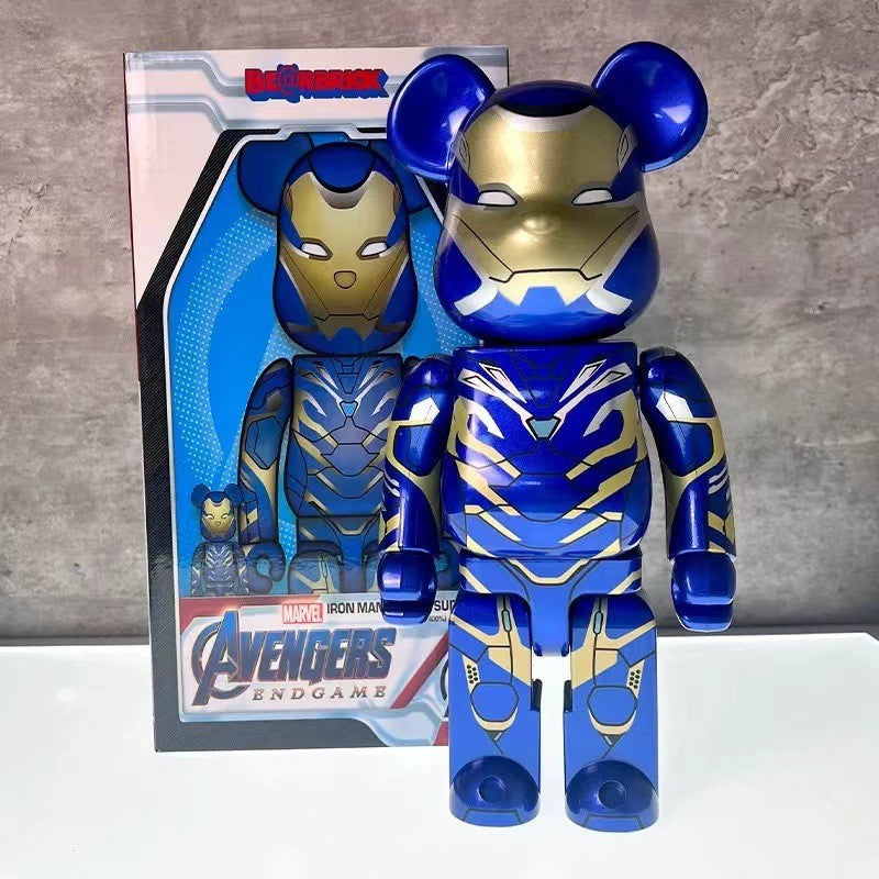 A blue and gold Marvel Avengers: Endgame Bearbrick toy figure stands in front of its retail box on a white surface against a gray wall.