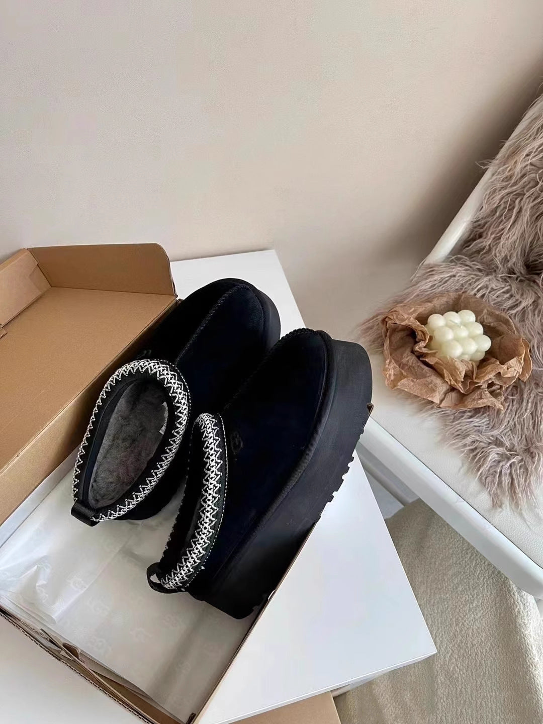 Black shoes with fuzzy texture on a white surface next to a cardboard box.