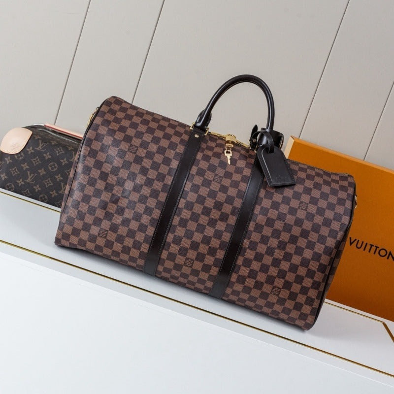 A Louis Vuitton monogram check duffel bag in brown and beige canvas with black leather handles and trim, displayed next to an orange Louis Vuitton box on a white surface.