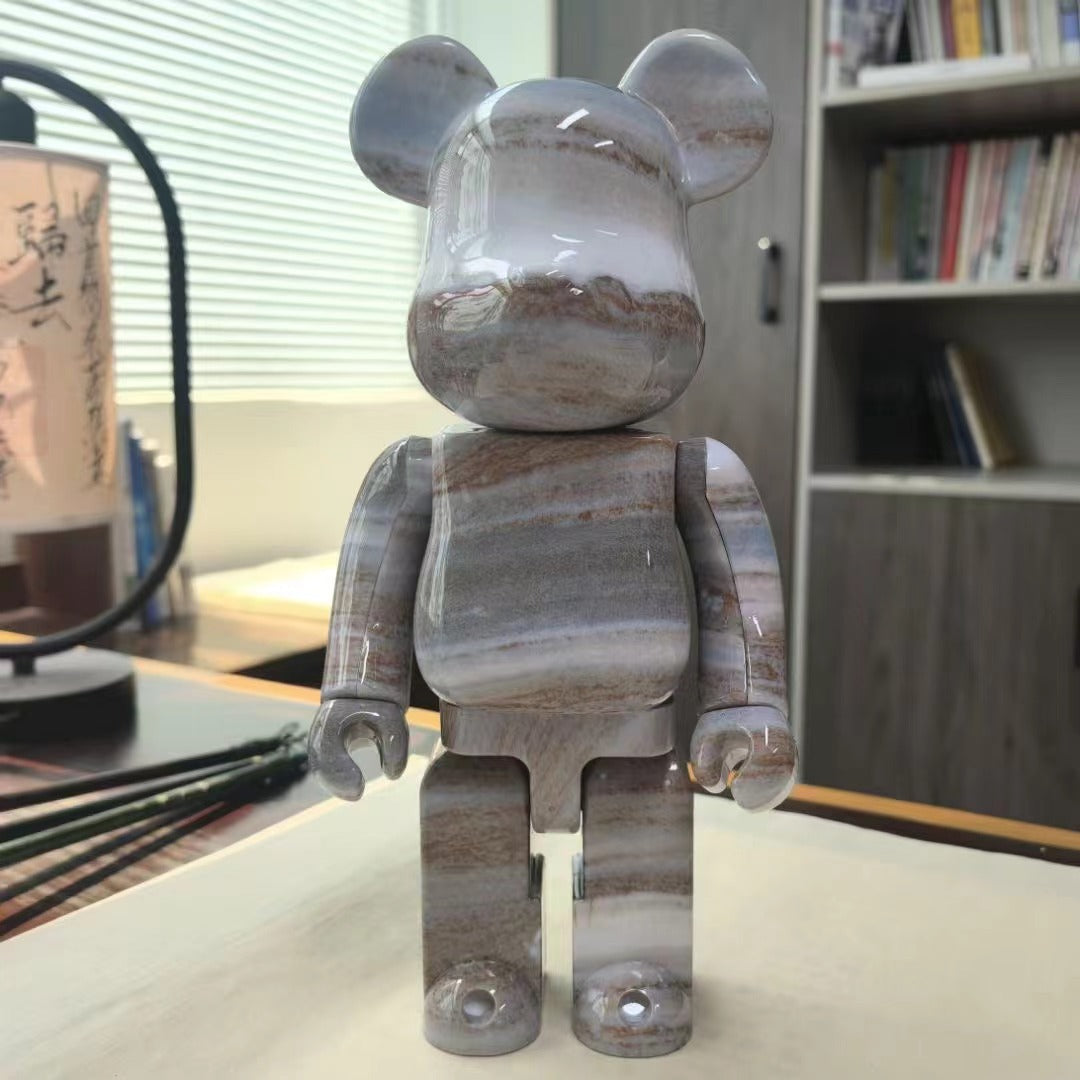 A bear-shaped collectible figure with a glossy marble-patterned body in gray, white, and brown tones, standing on a tabletop in an indoor room setting.