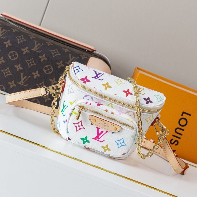 A small Louis Vuitton crossbody bag in white coated canvas with a colorful monogram print, gold-tone zippers, and a beige leather strap, styled on a white surface with a brown monogram wallet and orange Louis Vuitton box in the background.
