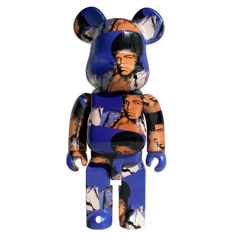 A collectible bear-shaped figure with a glossy blue and multicolor collage print featuring portraits, shown against a plain white background.