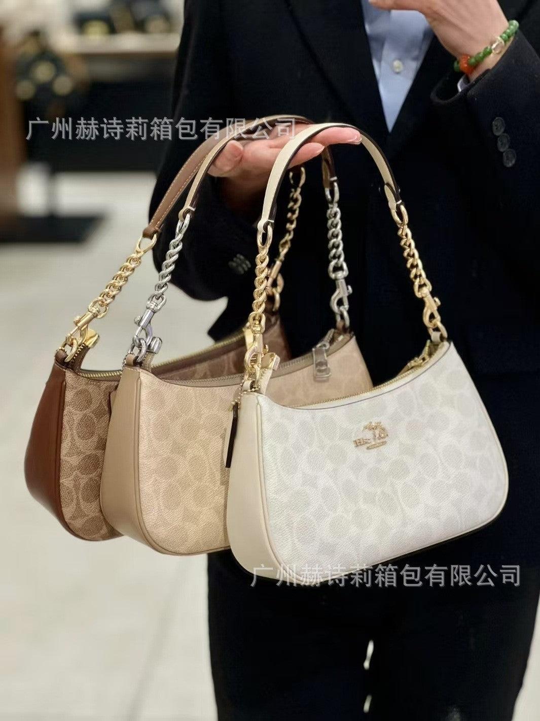 Three handbags in different colors held by a person wearing a dark suit.