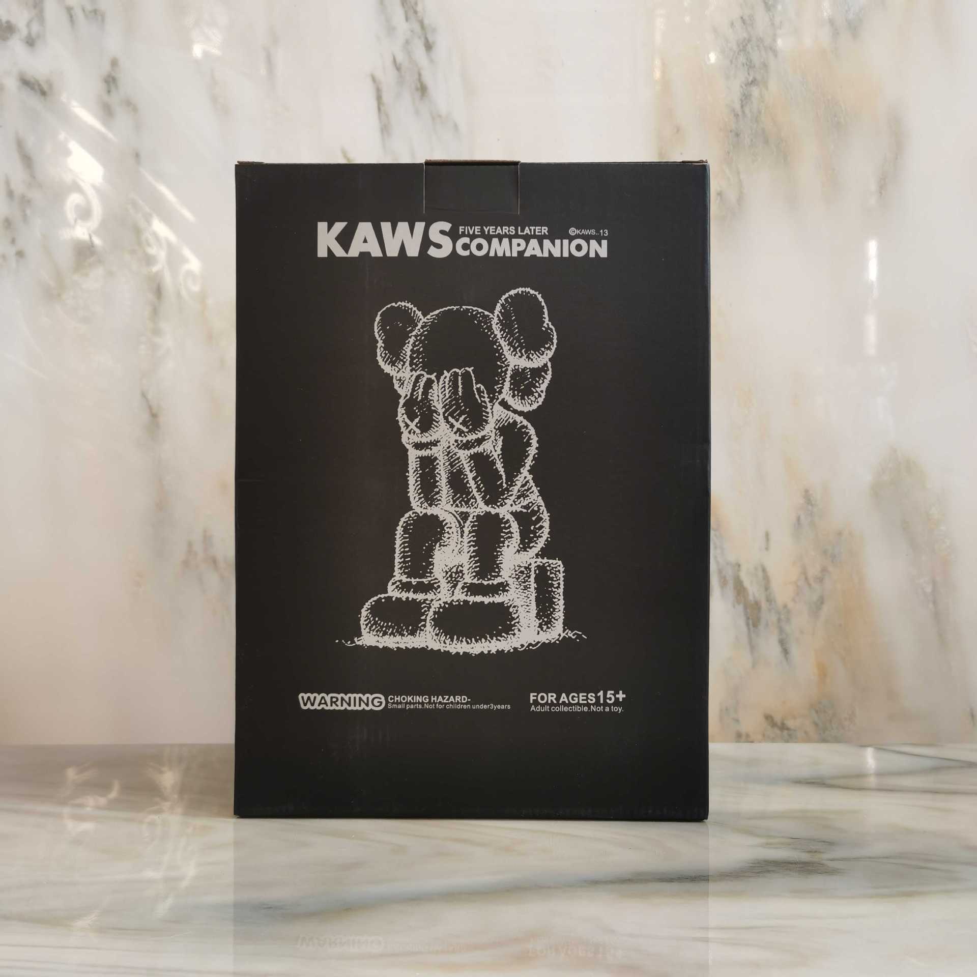 A black KAWS Companion box featuring a white chalk-style drawing of the Companion figure, standing on a marble surface against a marble background.