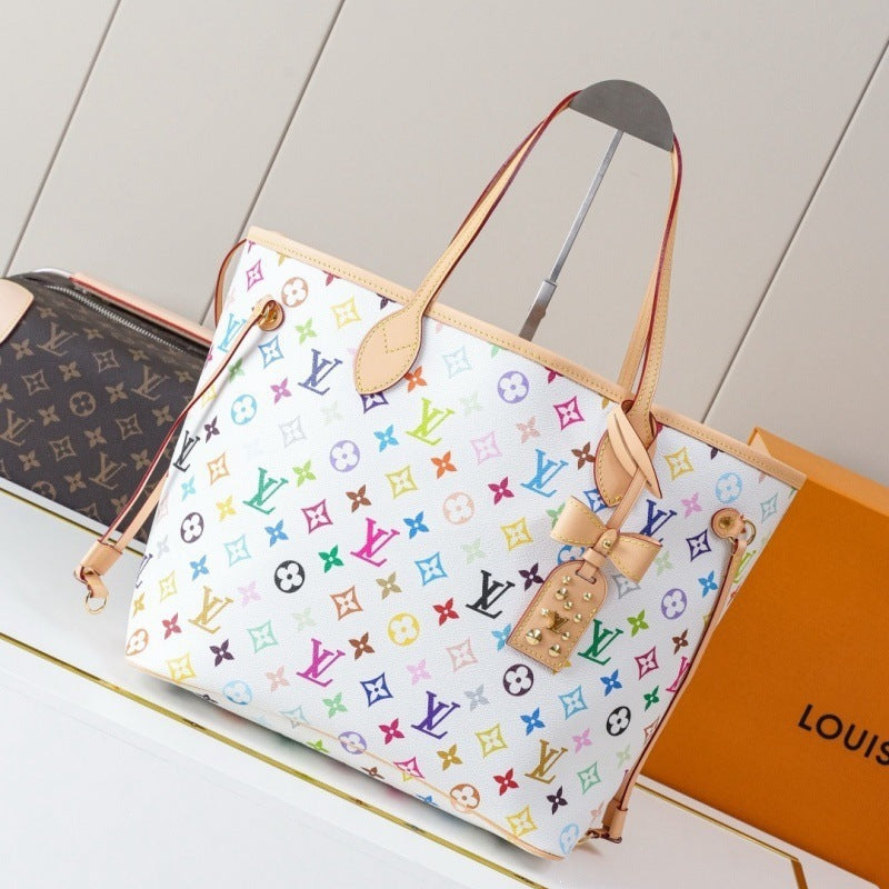 A Louis Vuitton Neverfull tote bag in white canvas with a colorful monogram pattern, featuring light tan leather handles and trim, displayed next to its orange Louis Vuitton box.