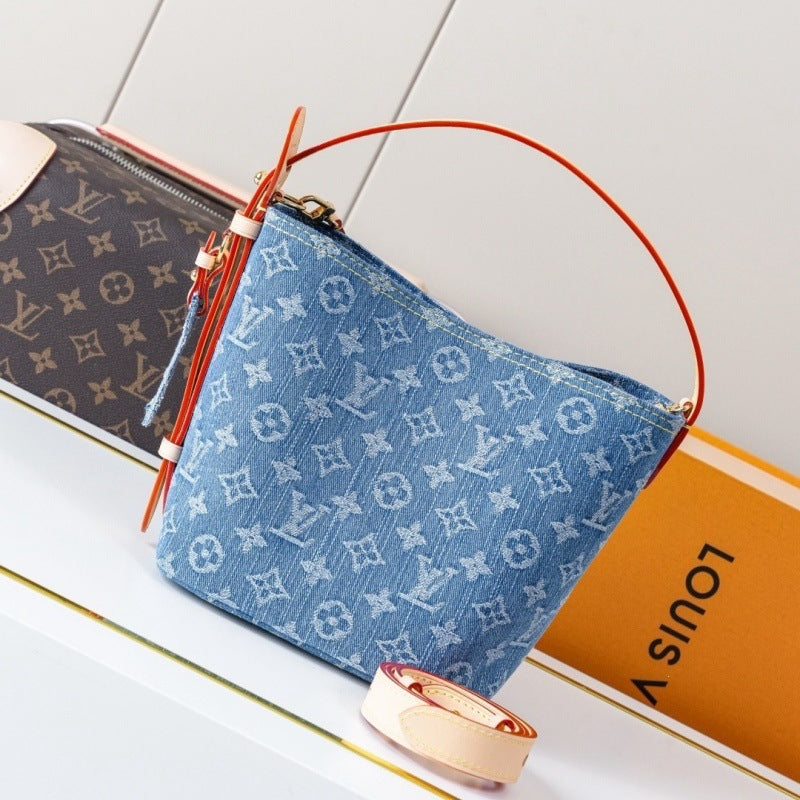 A Louis Vuitton monogram handbag in light blue canvas with a red leather handle, displayed next to an orange Louis Vuitton box on a white surface.