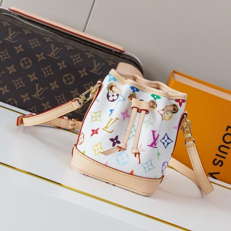 A Louis Vuitton mini bucket bag in the brand's classic multicolor pastel monogram canvas, styled on a white surface next to a Louis Vuitton monogram pouch and an orange box.