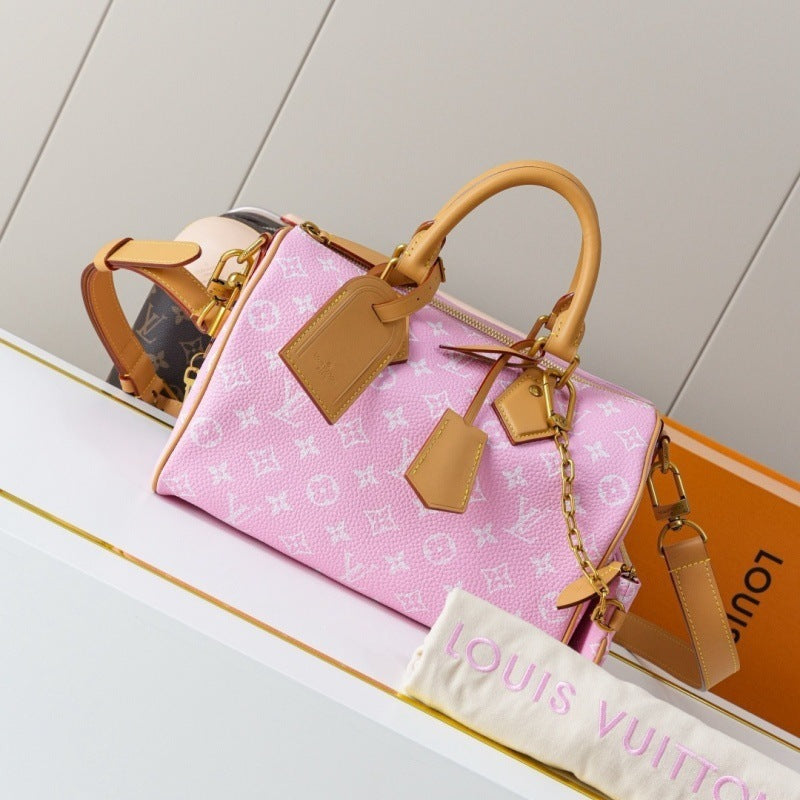 A pink Louis Vuitton monogram Speedy handbag with tan leather handles and tags, displayed on a white shelf next to an orange Louis Vuitton box and a white dust bag.