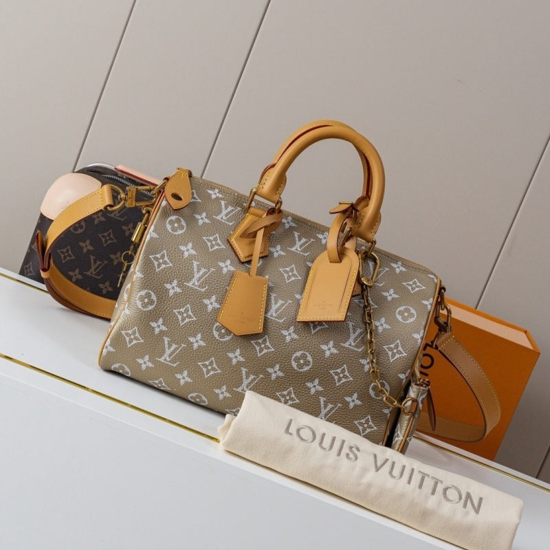 Louis Vuitton monogram Speedy handbag in beige canvas with tan leather handles and trim, displayed on a white shelf with a dust bag and orange box in the background.
