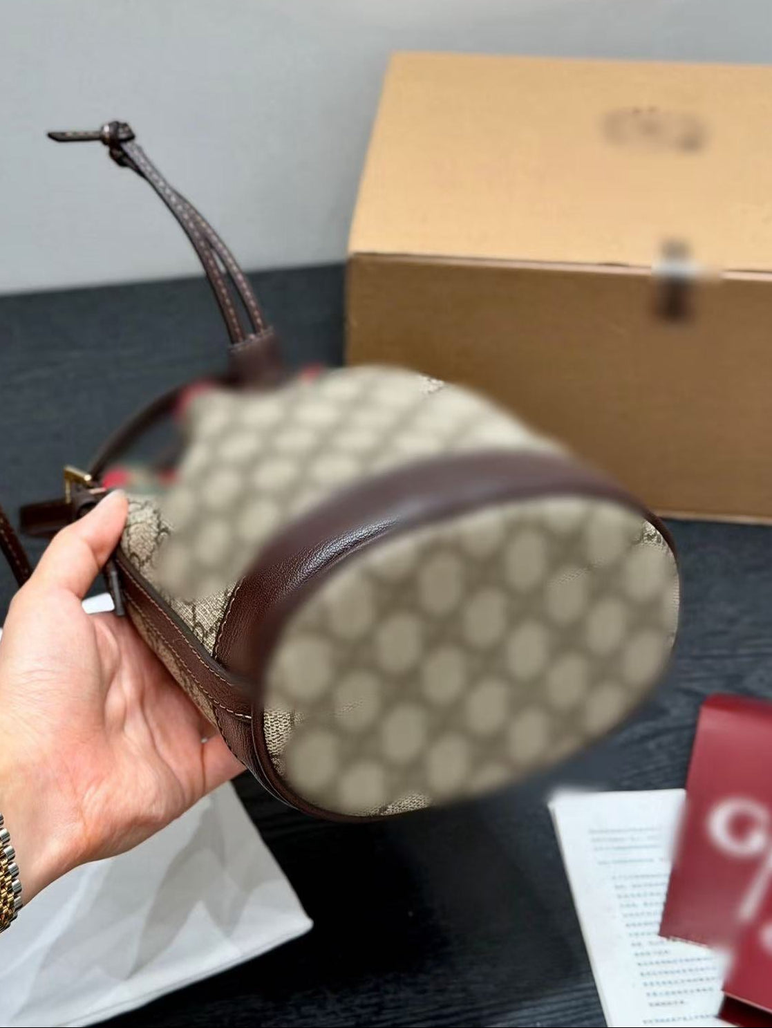 Hand holding a Gucci handbag with a box and paper in the background