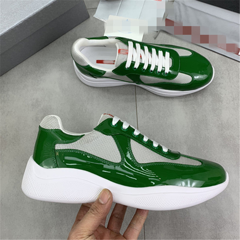 Green and white sneakers held by a hand on a gray floor.