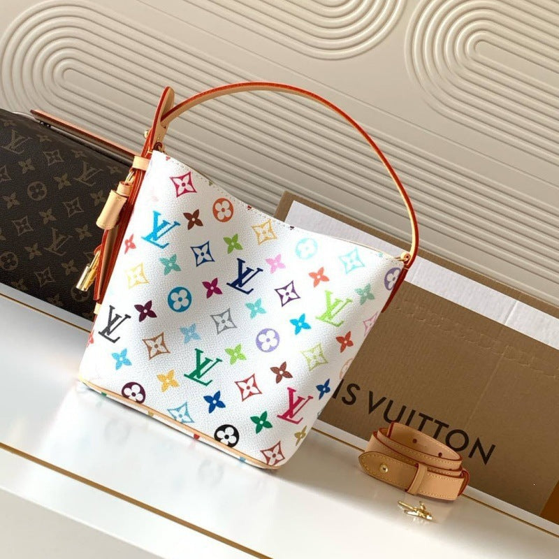 A Louis Vuitton handbag with a white canvas body covered in colorful monogram motifs, featuring a tan leather top handle and strap, displayed on a white surface with a branded box in the background.