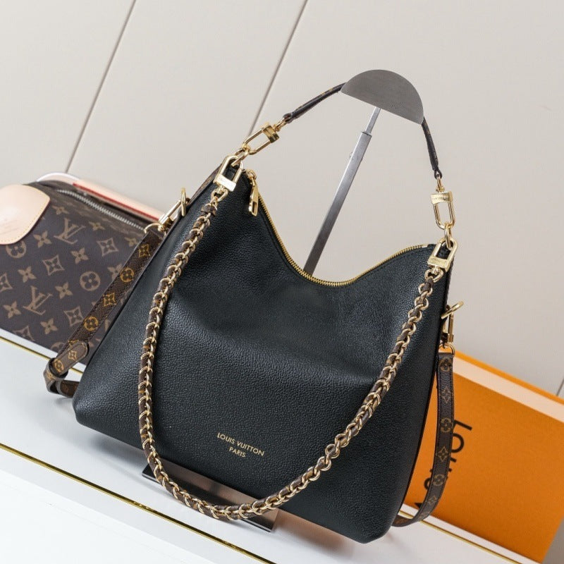 A black pebbled leather Louis Vuitton shoulder bag with gold-tone hardware, a chain strap, and a monogram-patterned detachable strap, displayed on a stand with a Louis Vuitton monogram box and orange packaging in the background.