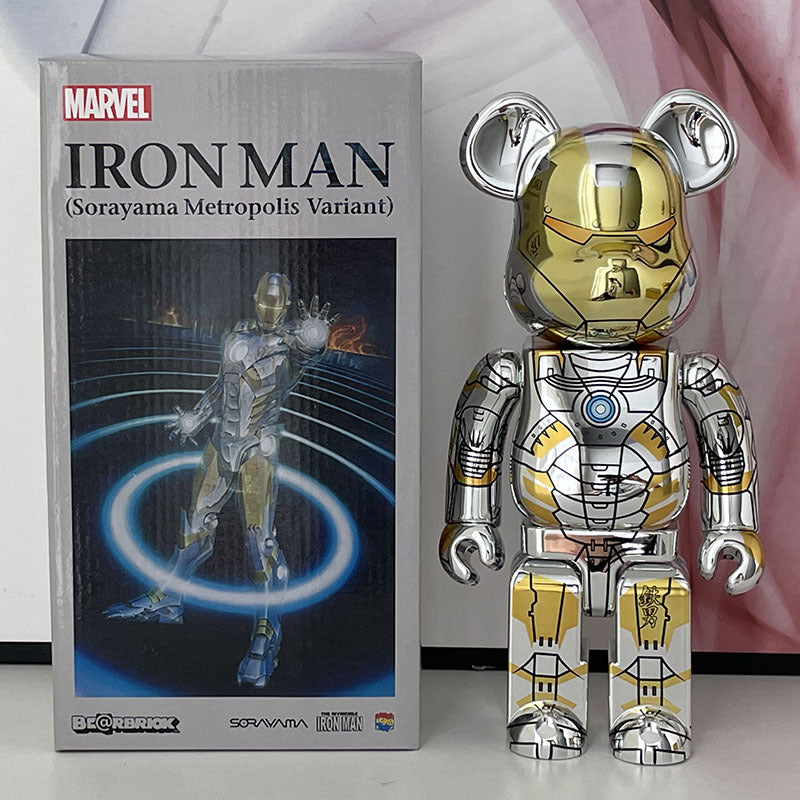 A metallic Iron Man toy figure stands next to its retail box. The figure has a chrome silver body with gold plating and a gold bear-head mask.