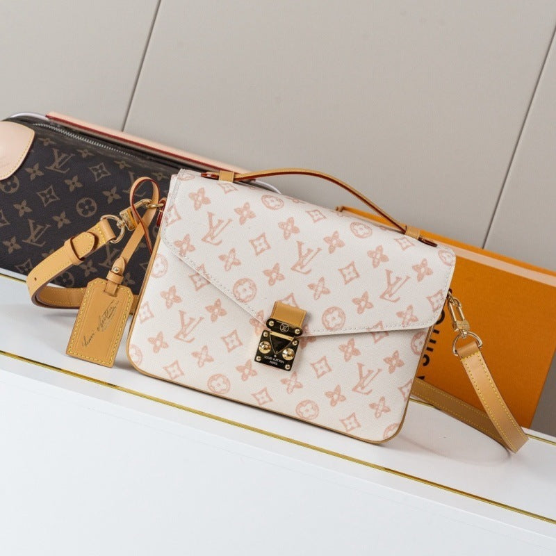 A Louis Vuitton shoulder bag in beige monogram canvas with tan leather trim and a gold-tone turn-lock clasp, displayed on a white shelf alongside other Louis Vuitton items.