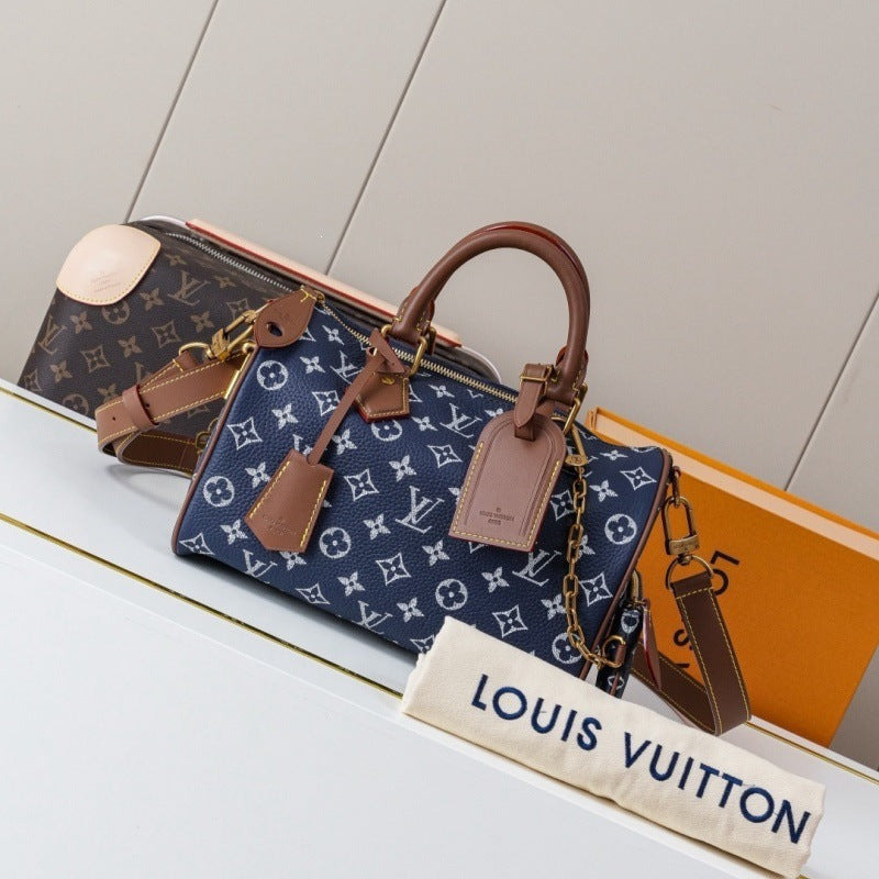 Louis Vuitton monogram canvas handbag in navy blue with brown leather handles and trim, displayed on a white surface with a dust bag and orange box in the background.