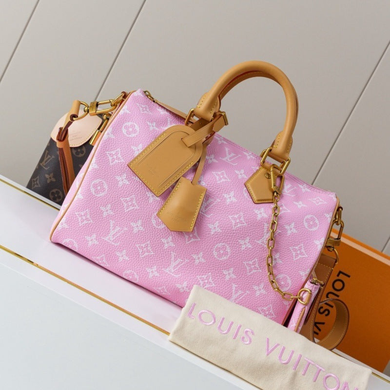 A pink Louis Vuitton monogram handbag with tan leather handles and a gold chain strap, displayed on a white shelf with a Louis Vuitton dust bag and branded box in the foreground.