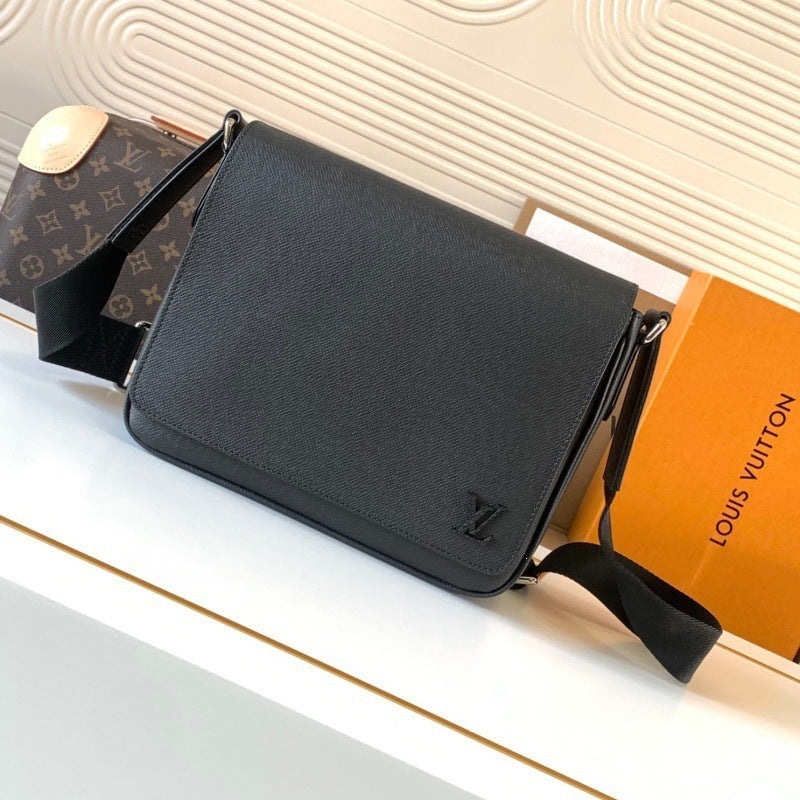 A black textured leather crossbody bag from Louis Vuitton, displayed on a white surface next to its signature orange box and a brown monogram clutch.
