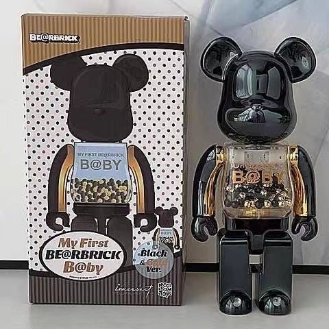 A glossy black Bearbrick Baby collectible figure standing next to its retail box. The box features a white background with black polka dots, a brown top and bottom border, and an illustration of the bear figure holding a glass jar of gold-colored beads.